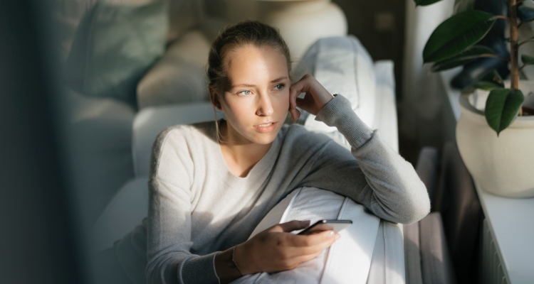 Serious teenage girl with cell phone sitting on couch at home