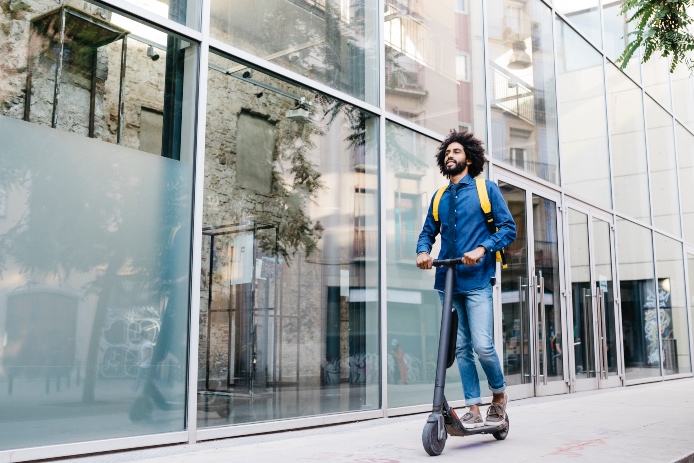 Man with backpack riding fast with his E-Scooter on pavement