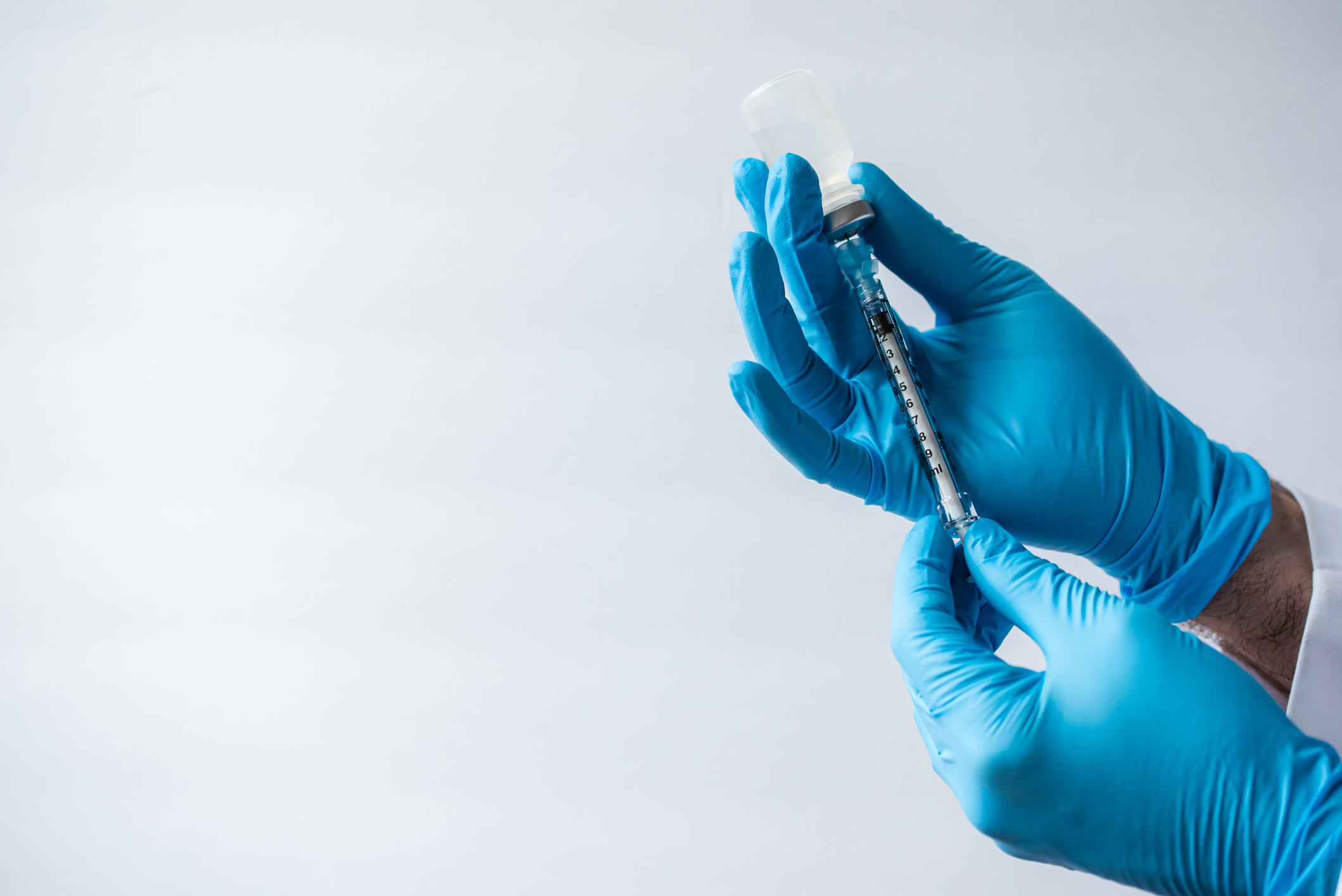 Hands in gloves drawing vaccine into syringe on white background.