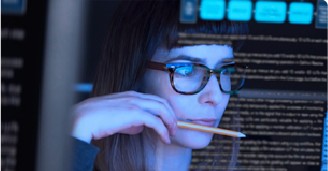 Mujer de negocios mira atentamente su pantalla de computador, donde se ve reflejado algunos textos